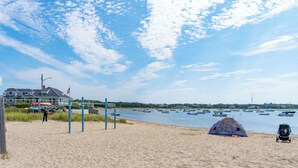 A beach with a tent, a fence, and a house in the background. - Cozy Cape Cod 17A with Fire Pit Near Beaches (Yarmouth)