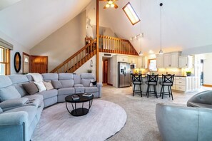 A spacious living area with a gray sectional sofa, a round coffee table, and a staircase leading to an upper level. - Serene Lake Pleasant House with Private Dock (Fremont)