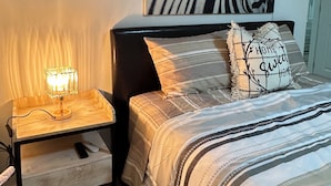 Een slaapkamer met een bed, een nachtkastje met een lamp, wanddecoratie met zebraprint, en een kussen met de tekst 'Home Sweet Home'.