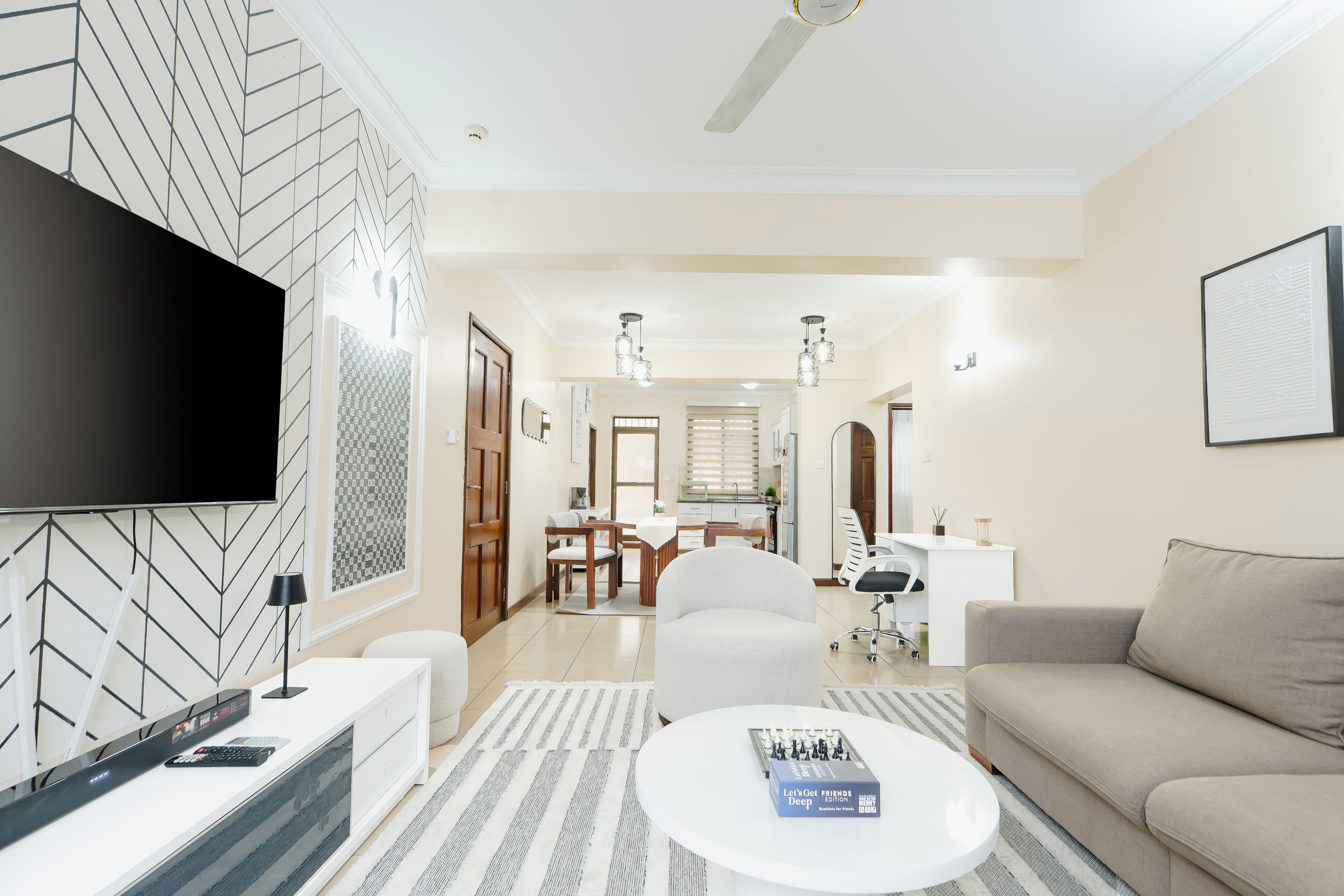 A modern living room with a flat-screen TV, a sofa, a coffee table, and a dining area with a table and chairs.