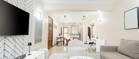 A modern living room with a flat-screen TV, a sofa, a coffee table, and a dining area with a table and chairs.