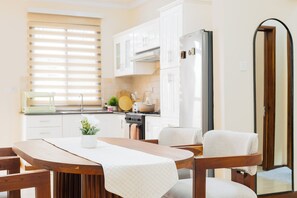 A modern kitchen with white cabinets, a wooden dining table, and a built-in oven. - Cozy 2BR, Fast Wi-Fi, GenSet, Workspace, Secure Gated Estate, 5mins to Beach (Dar es Salaam)