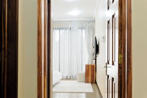Ein Hotelzimmer mit Bett, einem Holznachttisch, einem weißen Teppich und einem Fenster mit Vorhängen.