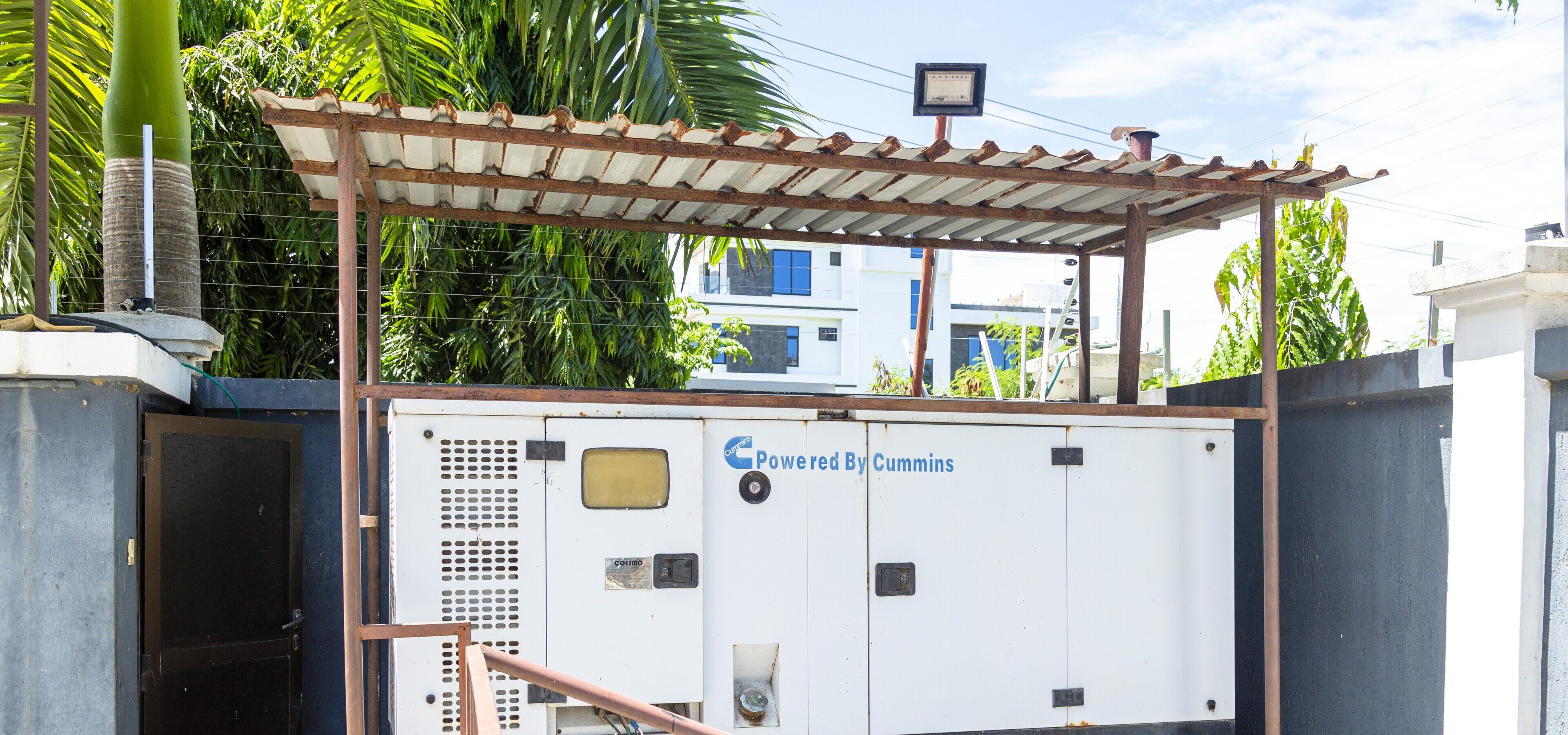 A utility room with a metal roof, a generator labeled 'Powered By Cummins,' and a metal gate.