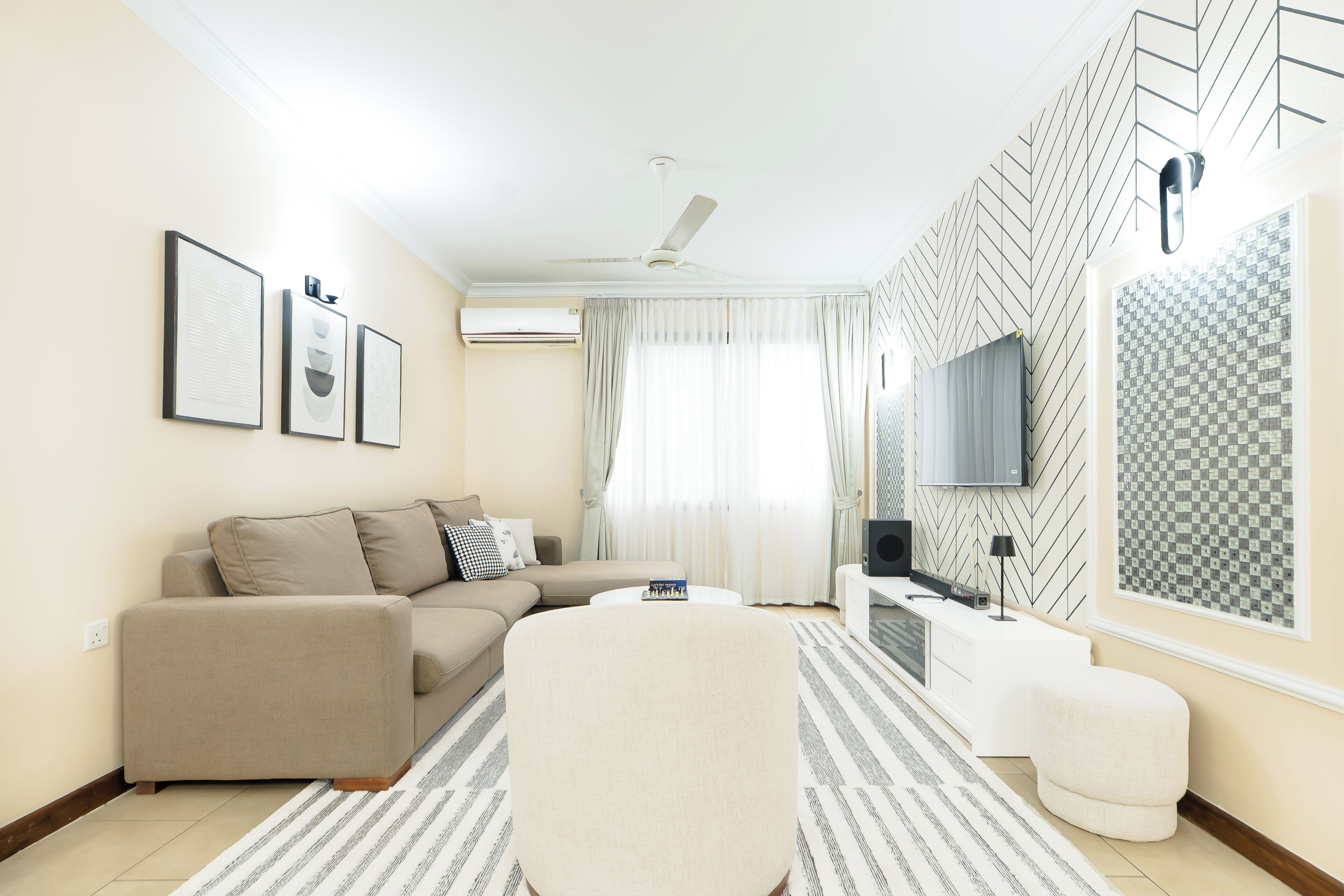 Una sala de estar moderna con sofá, reposapiés, televisor de pantalla plana y equipo de aire acondicionado.
