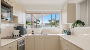 A modern kitchen with a built-in oven, a stovetop, a sink, and a window with a view of palm trees. - Coastal Comfort with a Private Spa Retreat (Margate)