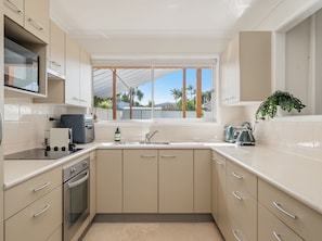 A modern kitchen with a built-in oven, a stovetop, a sink, and a window with a view of palm trees.