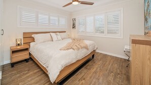 A bedroom with a wooden bed, white bedding, a ceiling fan, and white shutters on the windows. - Coastal Comfort with a Private Spa Retreat (Margate)