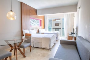 Ein modernes Hotelzimmer mit Glastisch, zwei Betten, einer Couch und einem großen Fenster.