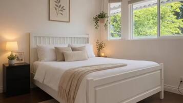 Een slaapkamer met een bed, nachtkastje, lamp en raam met uitzicht op groen.