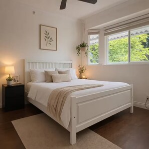 A bedroom with a bed, bedside table, lamp, and window with a view of greenery. - Sweet suite in Sophia’s home 201 (Vancouver)