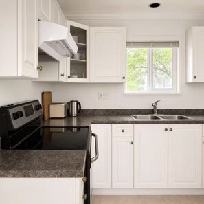 A kitchen with white cabinets, a black stove, a window, and a sink. - Sweet suite in Sophia’s home 201 (Vancouver)