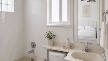 Een badkamer met bad, toilet, wastafel en een raam met zonwering.