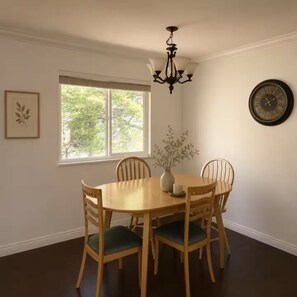 A dining room with a round table, four chairs, a chandelier, a window, and a wall clock. - Sweet suite in Sophia’s home 201 (Vancouver)