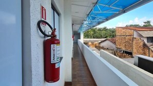 Un pasillo con un extintor colgado en la pared, una puerta y vistas a edificios exteriores.