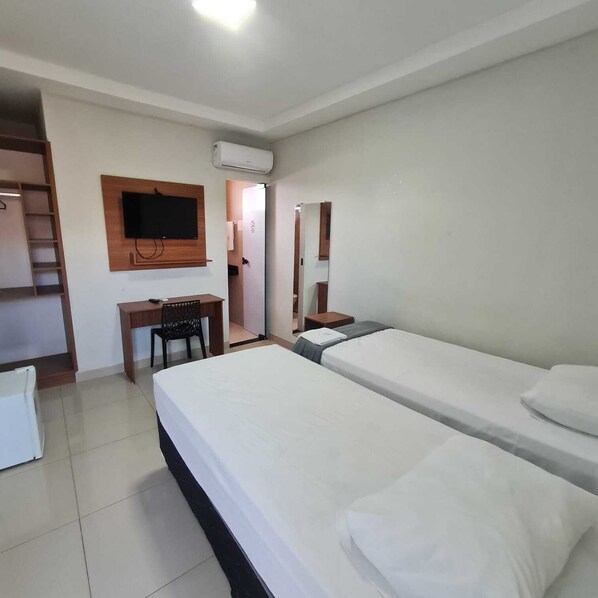 A hotel room with a bed, a desk, a chair, a TV, and an air conditioning unit. - BOTUS HOTEL (Barcarena)