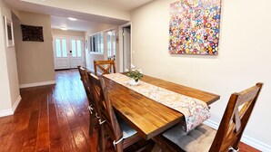 A dining area with a wooden table, chairs, and a colorful abstract painting on the wall. - UC Gem with Beautiful Yard (San Diego)