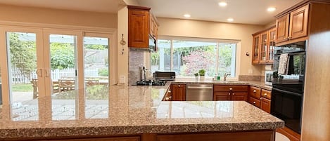 Una cocina con encimeras de granito, armarios de madera, microondas, estufa y lavavajillas.