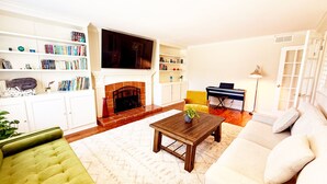 A living room with a fireplace, bookshelves, a television, a piano, and a sofa. - UC Gem with Beautiful Yard (San Diego)