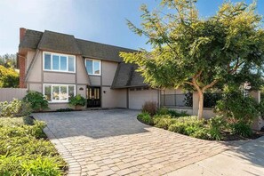 A two-story house with a paved driveway, a tree in the front yard, and a black gate. - UC Gem with Beautiful Yard (San Diego)