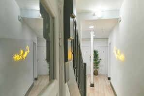 Un couloir moderne avec un escalier, une plante en pot et des enseignes lumineuses au néon sur les murs.
