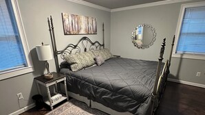 Ein Schlafzimmer mit Bett, Nachttisch, Lampe, Spiegel, Kunstwerk und Teppich.