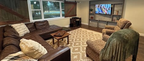 A living room with a sectional sofa, a patterned armchair, a coffee table, and a television on a wooden shelf.