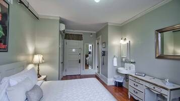 A hotel room with a bed, bedside table, lamp, dresser, mirror, and a bathroom with a sink and mirror.