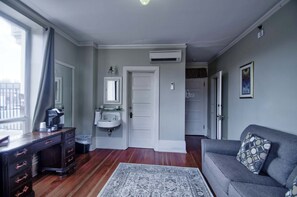 Een kamer met een bank, een koffiezetapparaat, een wastafel en een deur naar een andere kamer.