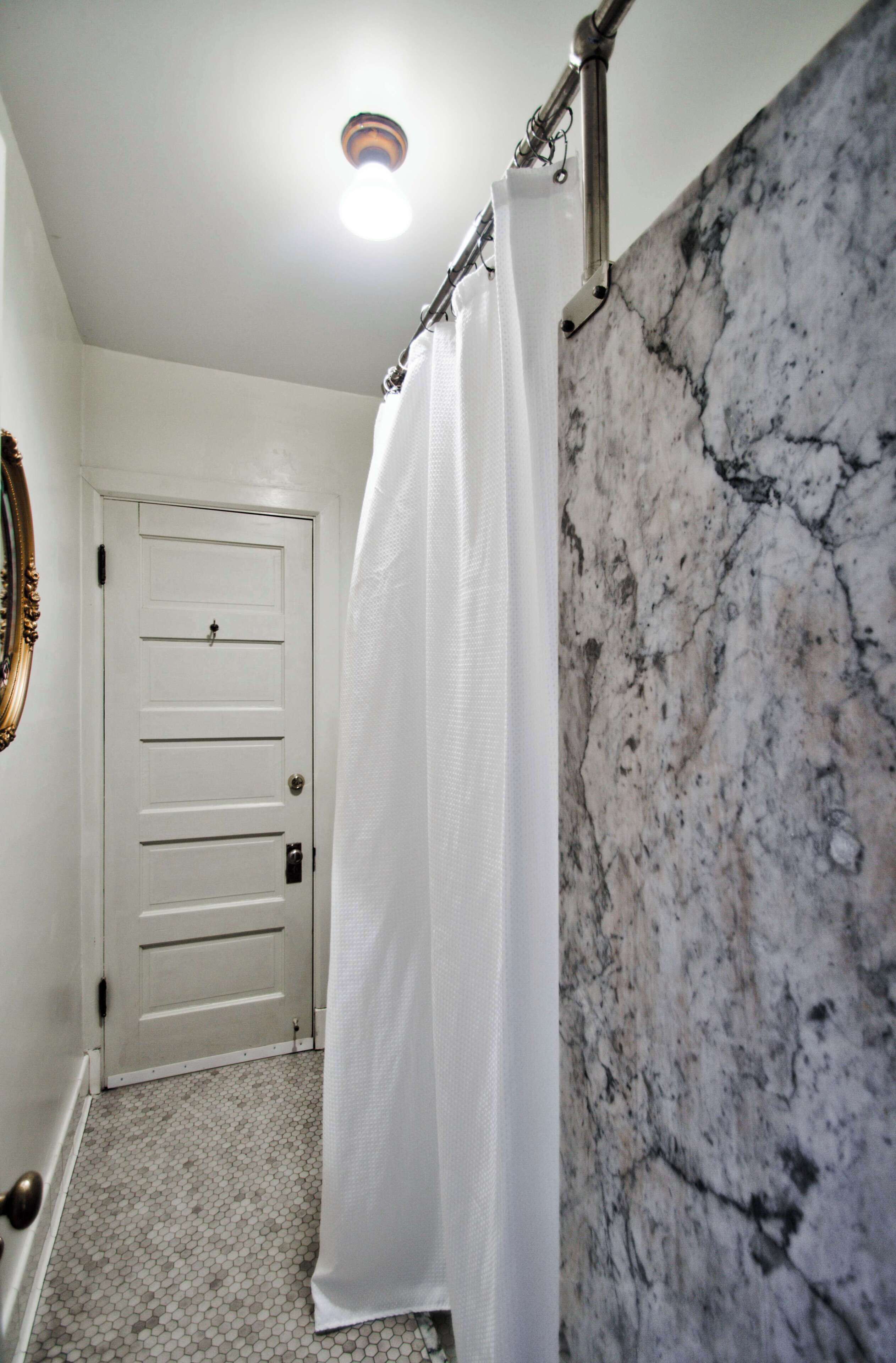 Un baño con puerta blanca, cortina de ducha y pared de mármol.