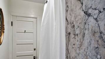 Un baño con puerta blanca, cortina de ducha y pared de mármol.
