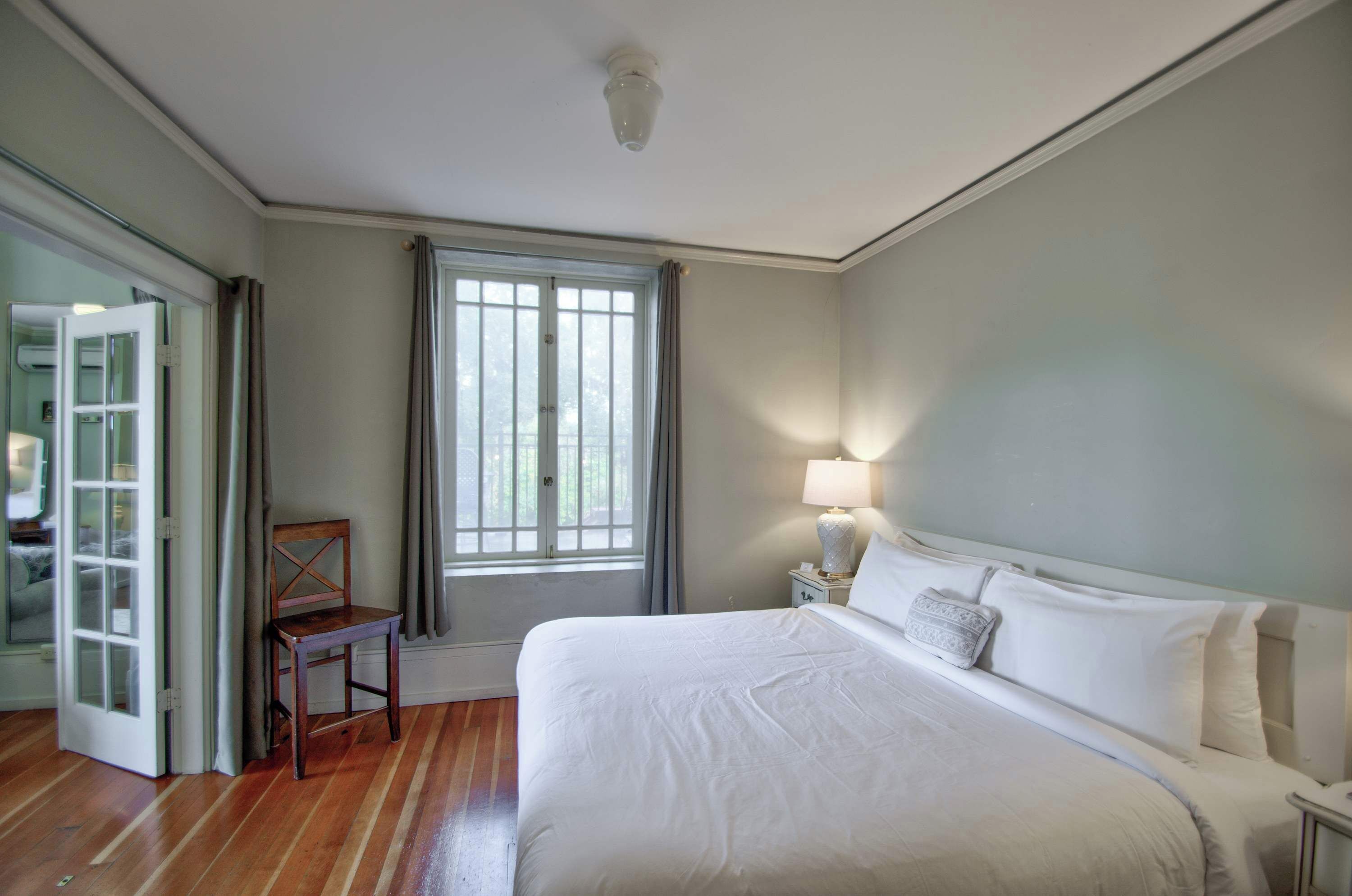 A bedroom with a bed, a chair, a window, and a nightstand with a lamp.