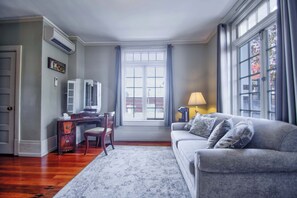 Una sala de estar con un sofá, un escritorio, una silla, una lámpara y una ventana con cortinas.