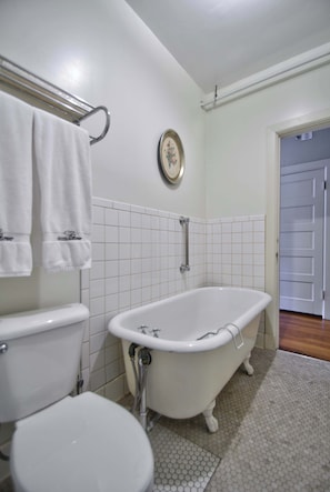 Un baño con inodoro, bañera y paredes de azulejos blancos.