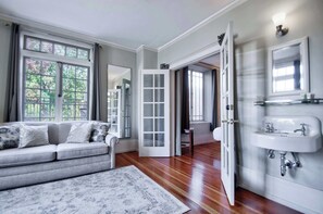A room with a grey sofa, a white rug, a wooden floor, a white door, and a white sink. - The Peak at Centralia Square | Historic Suite 201 (Centralia)