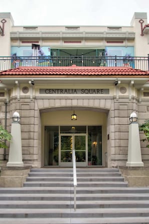 Un edificio con un cartel que dice 'CENTRALIA SQUARE' en la entrada, con techo de tejas rojas, un balcón con barandilla y una escalera que lleva a la entrada.