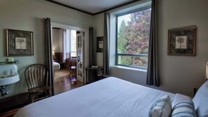Ein Schlafzimmer mit einem großen Bett, einem Fenster mit Blick auf Bäume, einem Sessel, einem kleinen Tisch und einem Waschbecken.