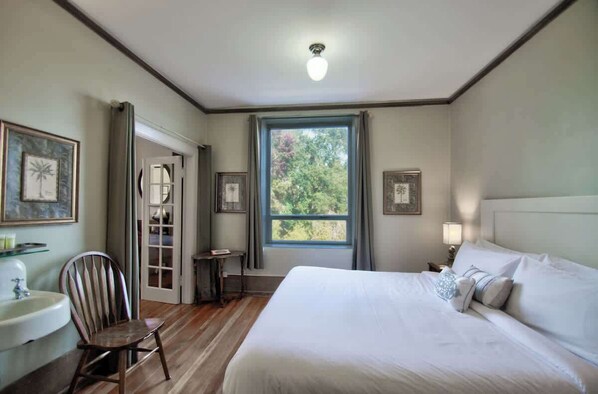 A bedroom with a bed, a chair, a nightstand, a lamp, a window, and a door.