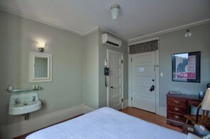 A bedroom with a bed, a bedside table, a mirror, a wall-mounted air conditioner, a door, and a framed picture.