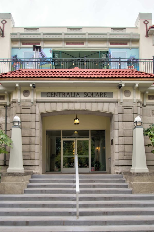 A building with a sign reading 'CENTRALIA SQUARE' at the entrance, featuring a red-tiled roof, a balcony with railings, and a staircase leading up to the entrance.