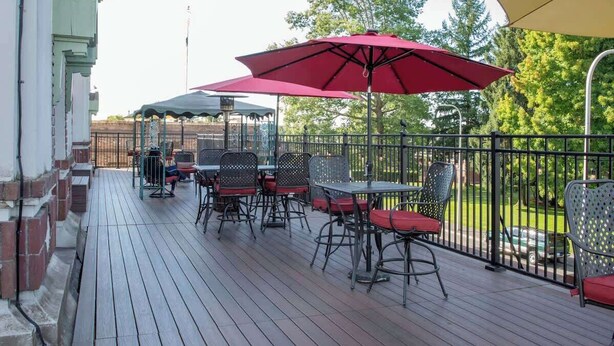 A wooden deck with outdoor seating, including tables and chairs, and red umbrellas providing shade. - The Peak at Centralia Square | Room 308 (Centralia)