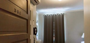 A hotel room with a door labeled '308,' a telephone, and a window with curtains.