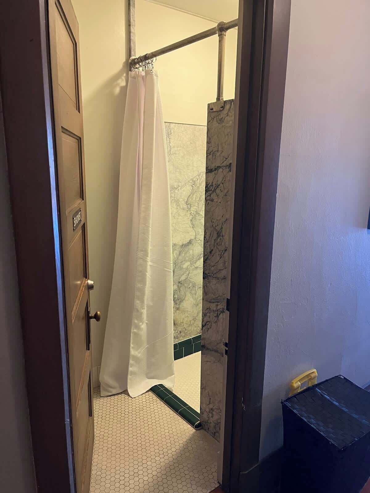 A bathroom with a shower curtain, a towel rack, a toilet, and a trash bin.