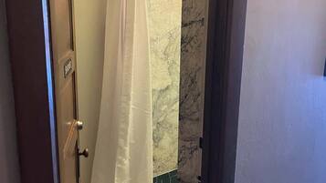 A bathroom with a shower curtain, a towel rack, a toilet, and a trash bin.