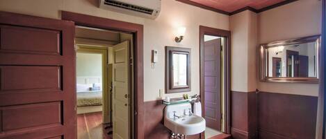 A hotel bathroom with a wooden floor, a white sink, a mirror, and an air conditioning unit.