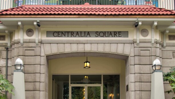 Un edificio con un letrero que dice 'CENTRALIA SQUARE' sobre la entrada, un conjunto de escaleras que conducen a la entrada y un balcón con barandillas.