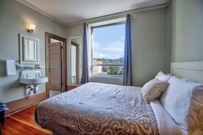 Un dormitorio con cama, ventana con cortinas, lavamanos y espejo.