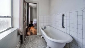 Un baño con bañera, ventana y puerta que da a un dormitorio.