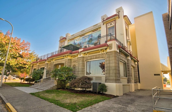 A two-story building with a balcony, a staircase, and a small garden area.