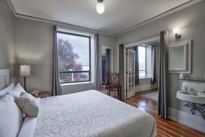 A hotel room with a large bed, a bedside table with a lamp, a bathroom with a sink and mirror, and a view through a window.